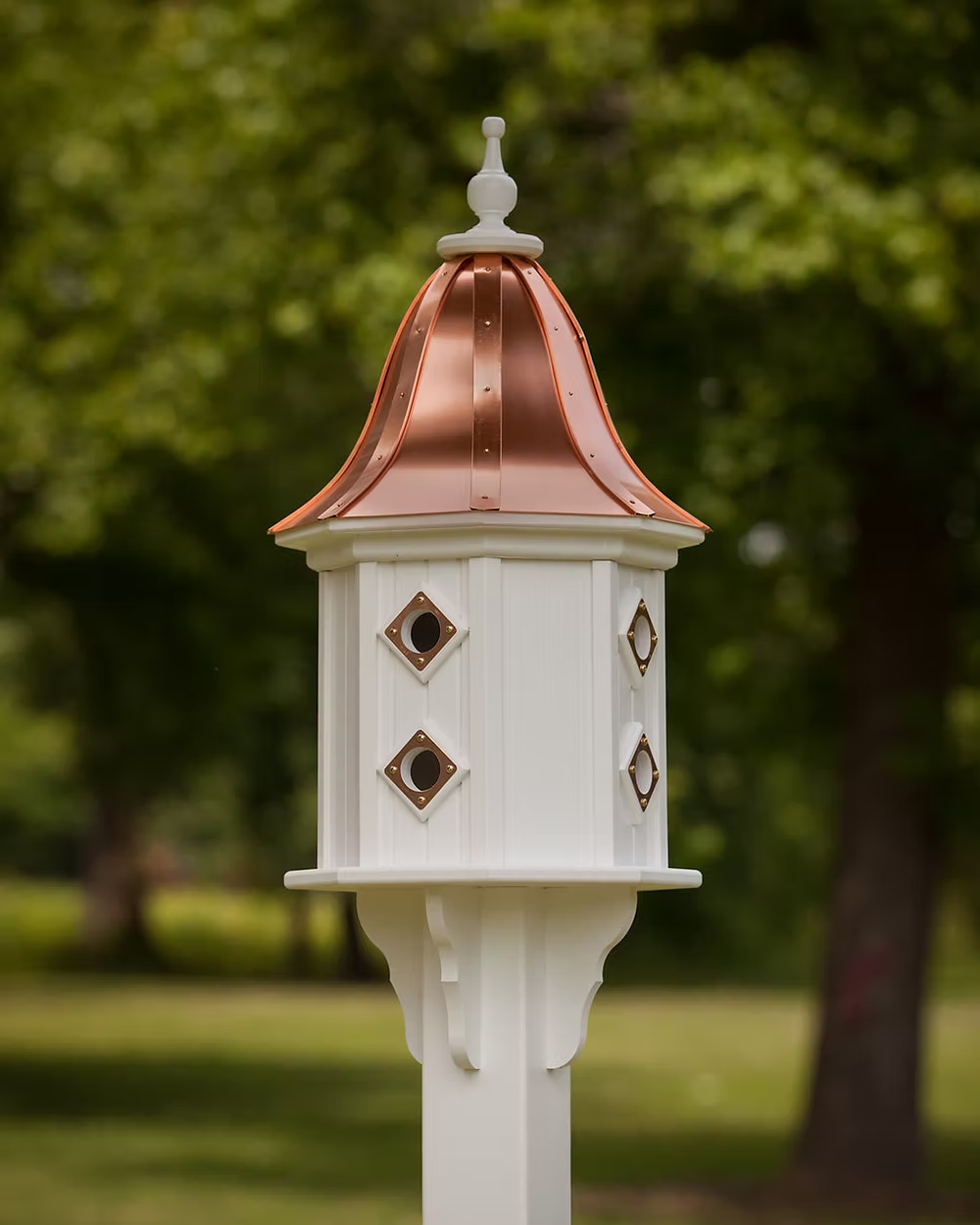 Decorative white birdhouse with a copper roof against a blurred green outdoor background